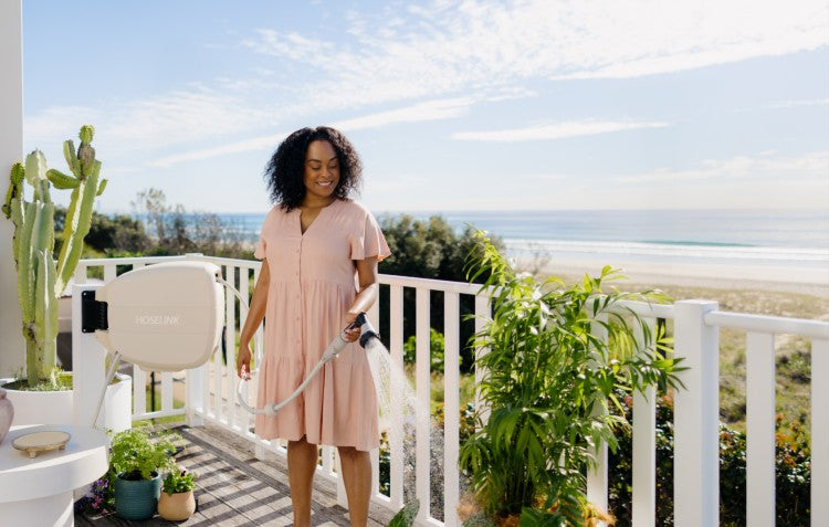 woman watering plants on the balcony with the beach in the background