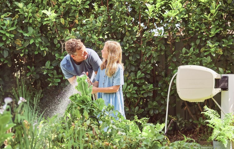 father and daughter using beige evolve hose reel to water veggie bed