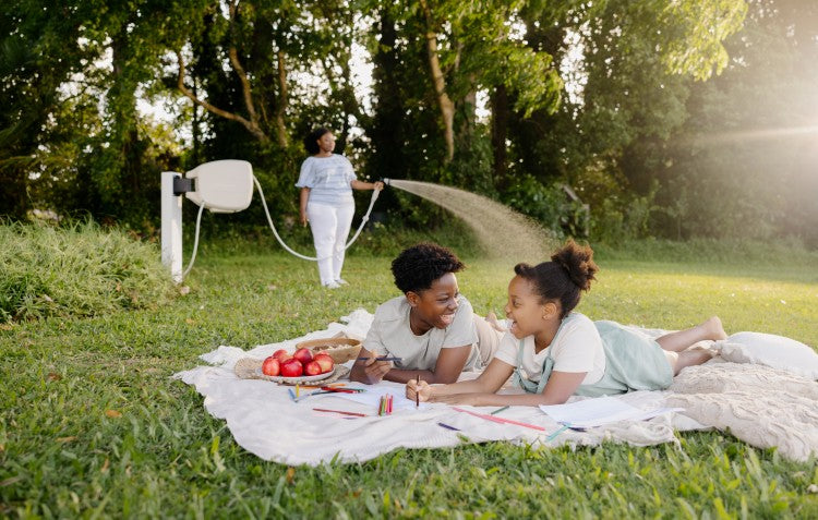 children enjoying picnic on lawn while their mother waters in the background