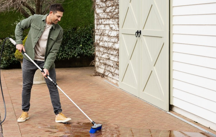 man using firm bristle brush to clean pavers