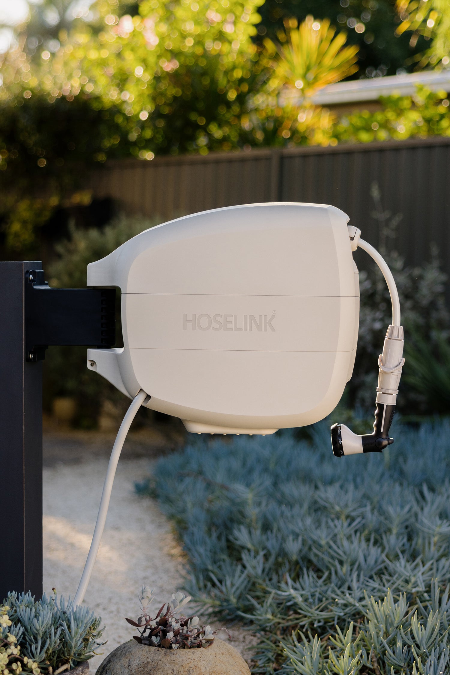 Beige Evolve™ Retractable Hose Reel on black post in garden planted with succulents