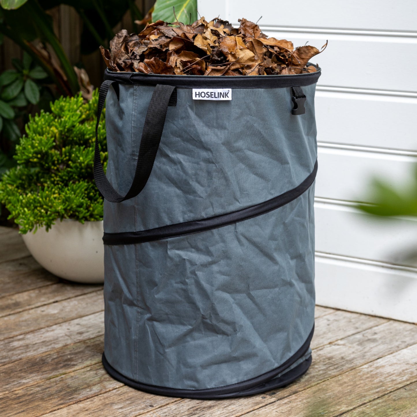 Charcoal coloured Pop up Waste Bag full of brown leaves sitting on a wooden deck