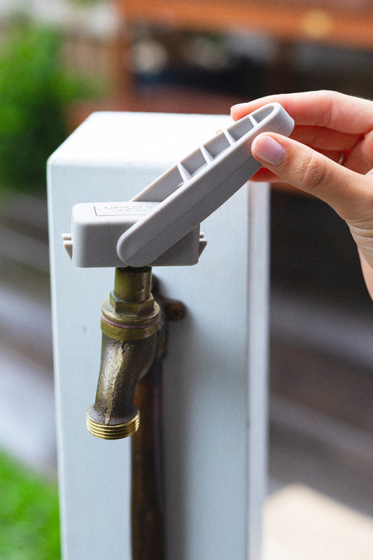 Warm grey Easy Tap Turner being used while attached to a brass outdoor tap mounted on a white timber post