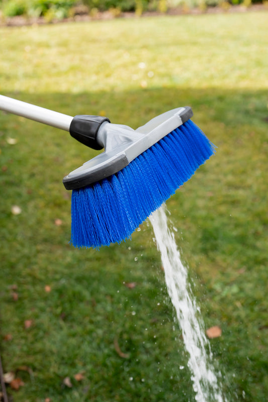 Close-up of the end of a cleaning brush with blue bristles and water shooting out of the end
