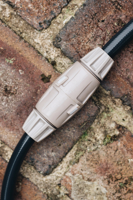Two warm grey Hose End Connectors joined together a charcoal hose laying across weathered brick paving. 
