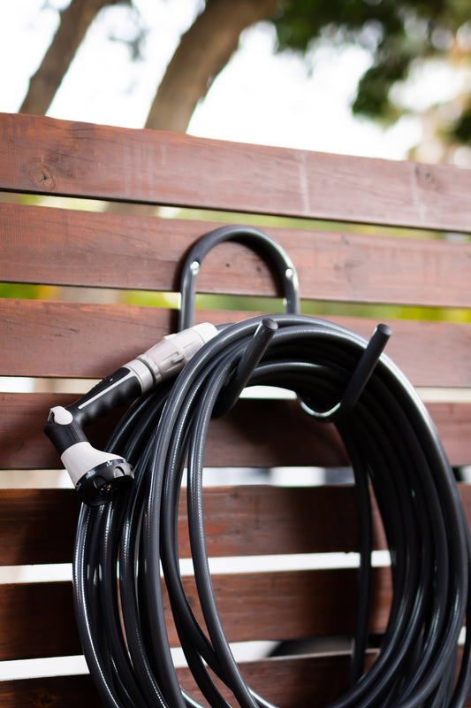 Charcoal metal hose hanger installed on wooden fence with charcoal Superflex Hose wrapped around it