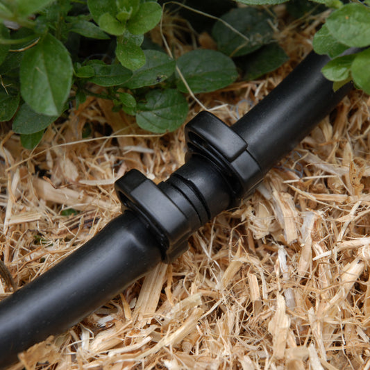 Cloes-up of black irrigation joiner secured in place with two 13mm ratchet clamps laying straw mulch