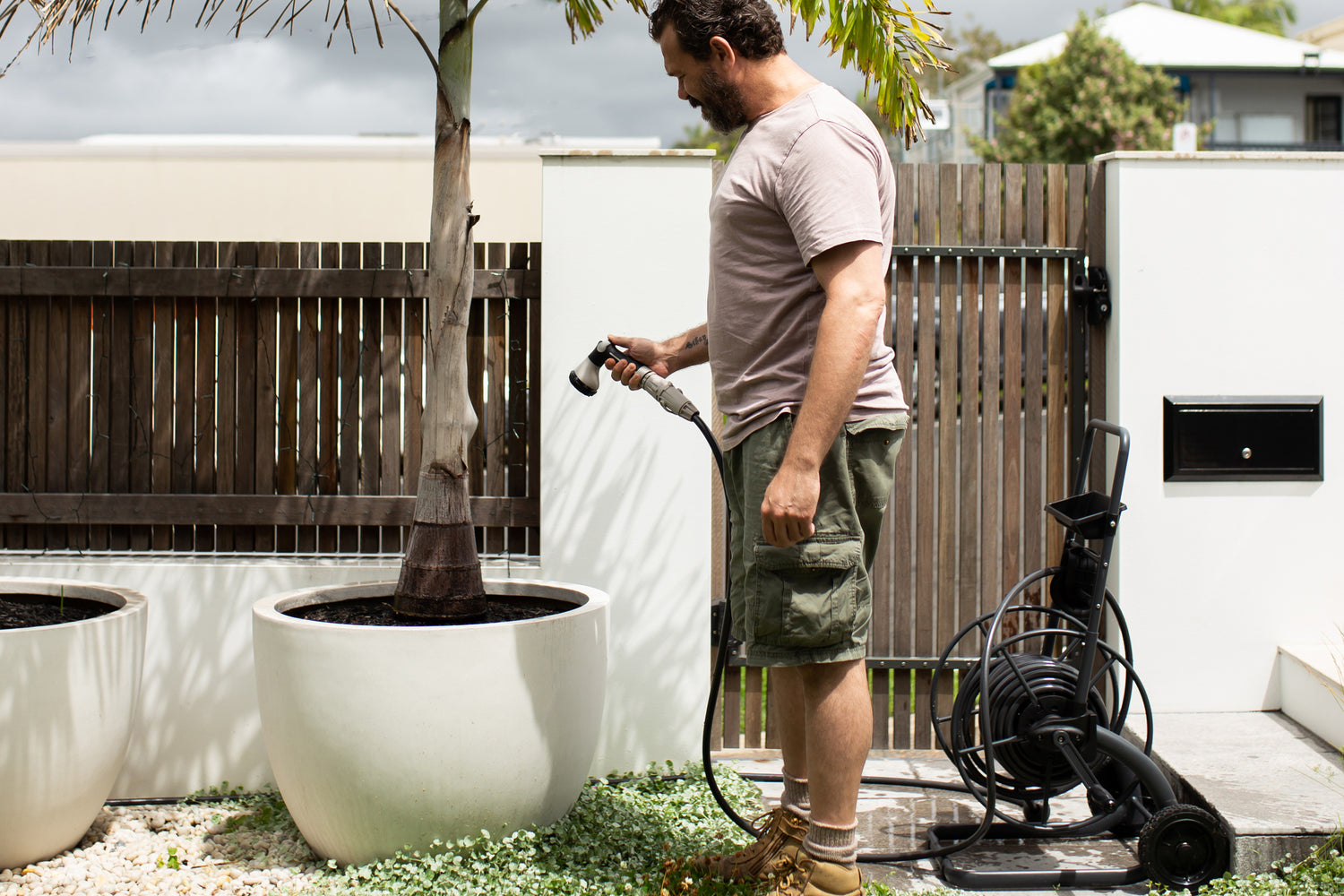 Man Watering His Potted Tree Using The Metal Hose Reel Cart
