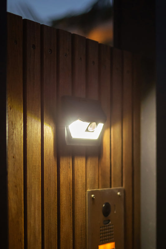 Small solar wall light turned on and mounted to a wall illuminating the door number