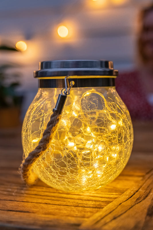 Glass crackle solar jar light turned on at night set on a garden table