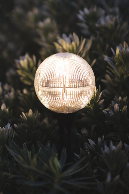 Close-up of Solar Garden Globe Light turned on at night staked into a bush 