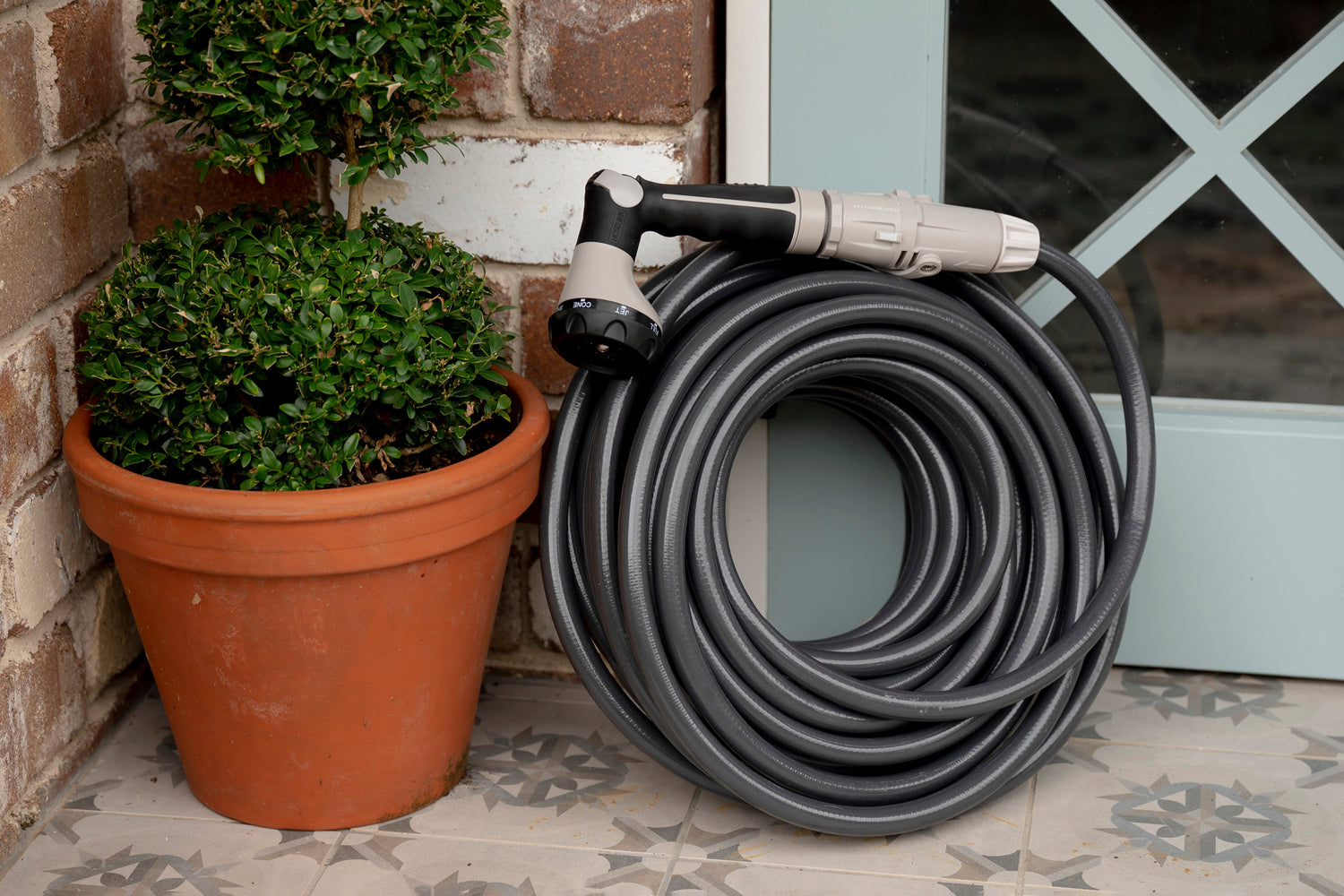 Superflex Charcoal Hose coiled leaning against a blue doorframe, next to pot plant