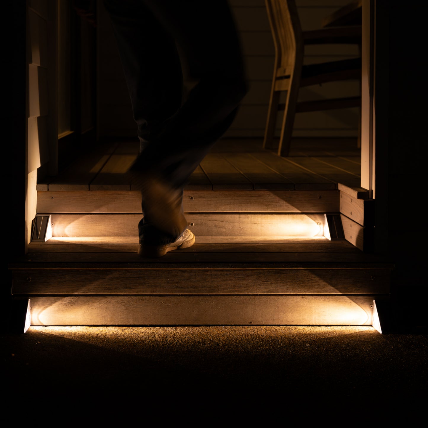 Person walking up a set of wooden stairs lit in warm white light by corner step lights