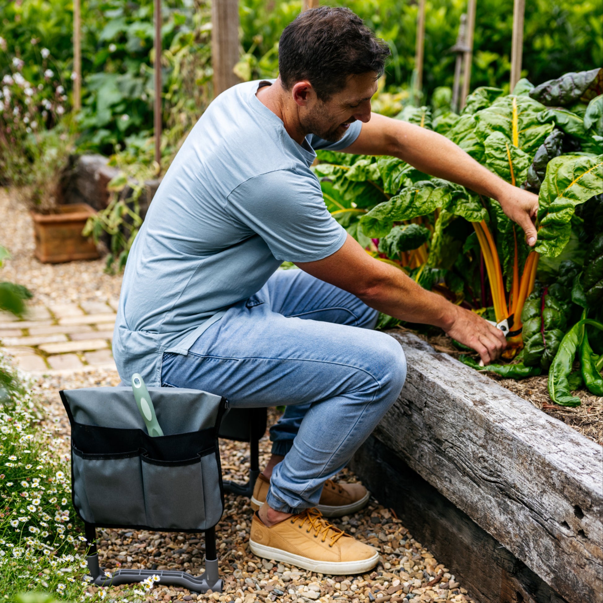 Person in blue shirt sitting on Folding Garden Kneeler & Seat with Tool Pouches next to a garden bed pruning plants