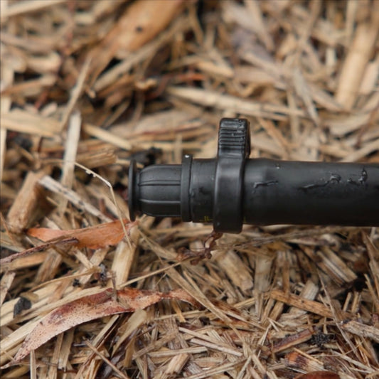 irrigation end cap installed into the end of black poly pipe secured in place with ratchet clamp on top of straw mulch