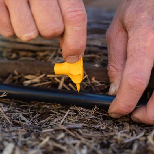 Person using a yellow key punch to create a hole in black pipe in a natural settinge