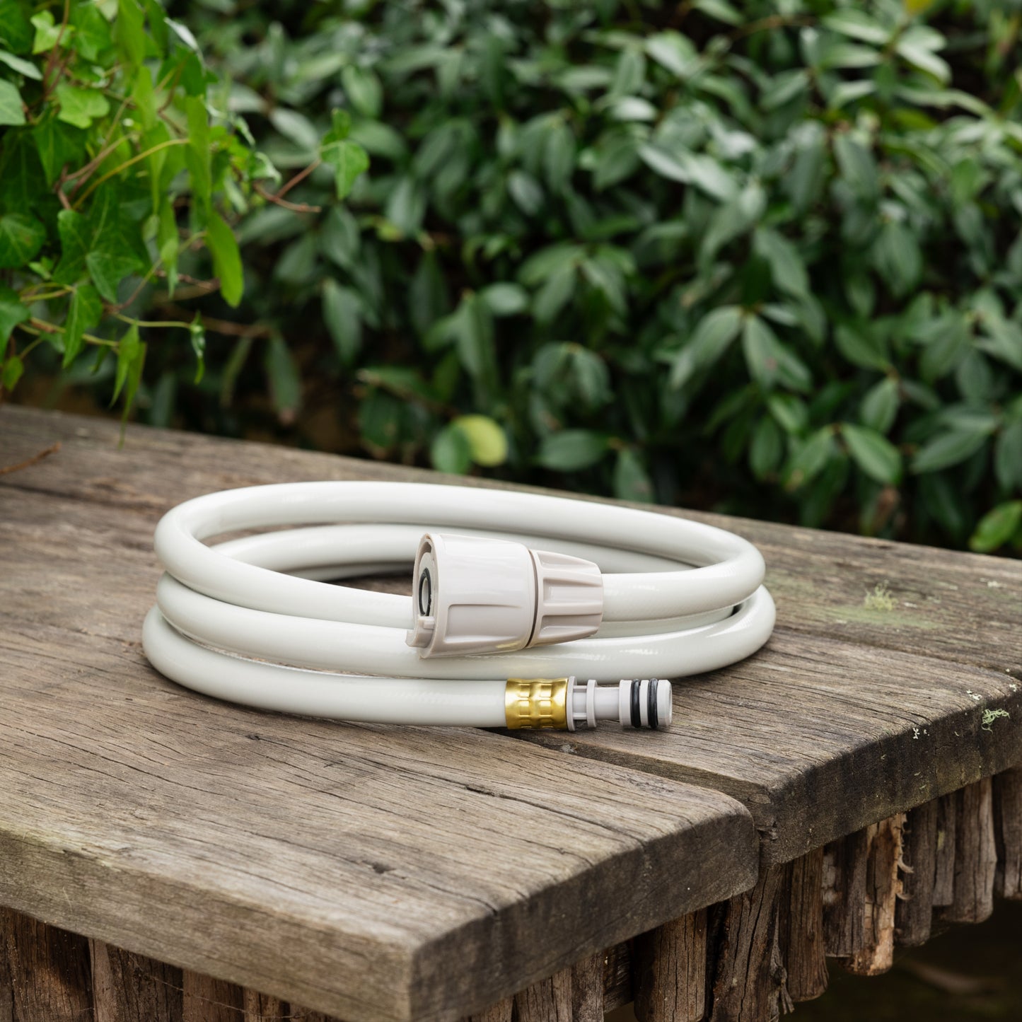 Coiled beige leader hose replacement sitting on a weathered wooden table with green hedges in the background
