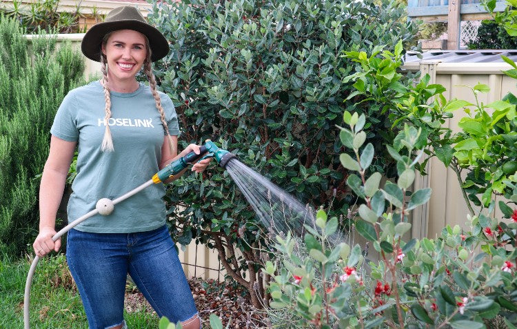 Gardener watering a Feijoa tree with a retractable hose reel