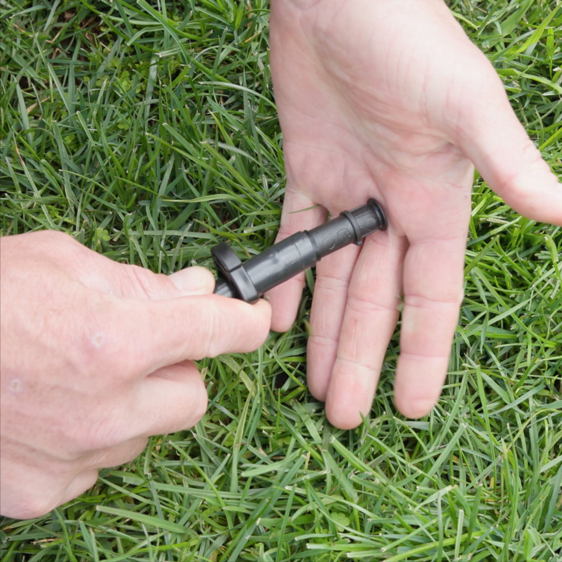 close-up pf person pushing irrigation end cap into black poliy pipe with green grass in the background