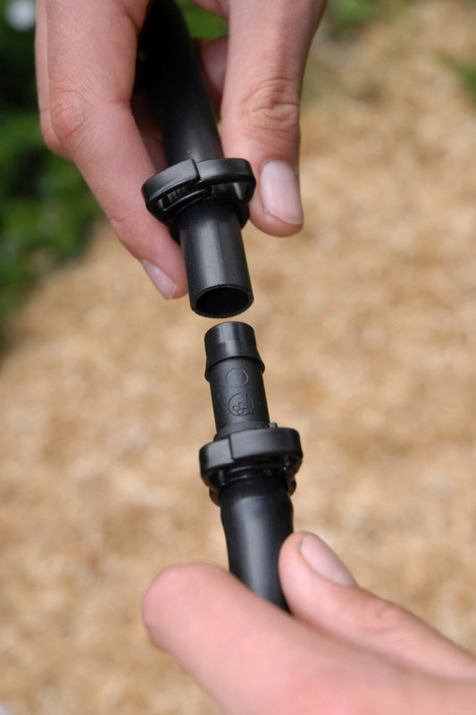close-up of hands installing a 13mm irrigation joinr to a piece of black poly pipe with ratchet clamps