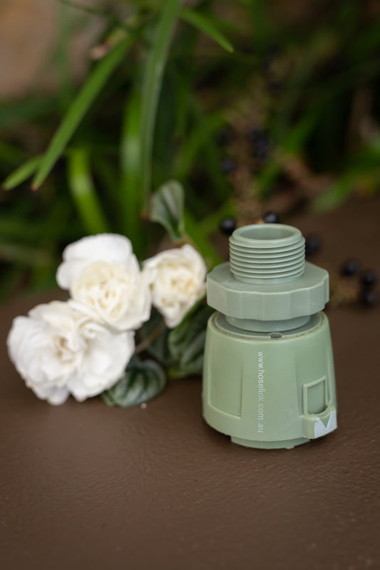 18mm commercial size green hose accessory connector with swivel placed on a wall next to cream flowers