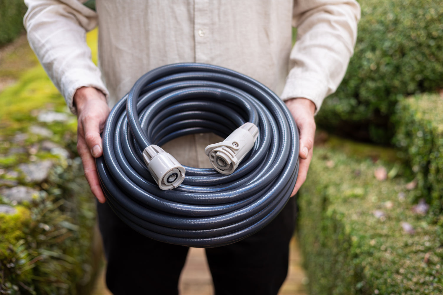 Person holding a coiled charcoal garden hose in an outdoor setting