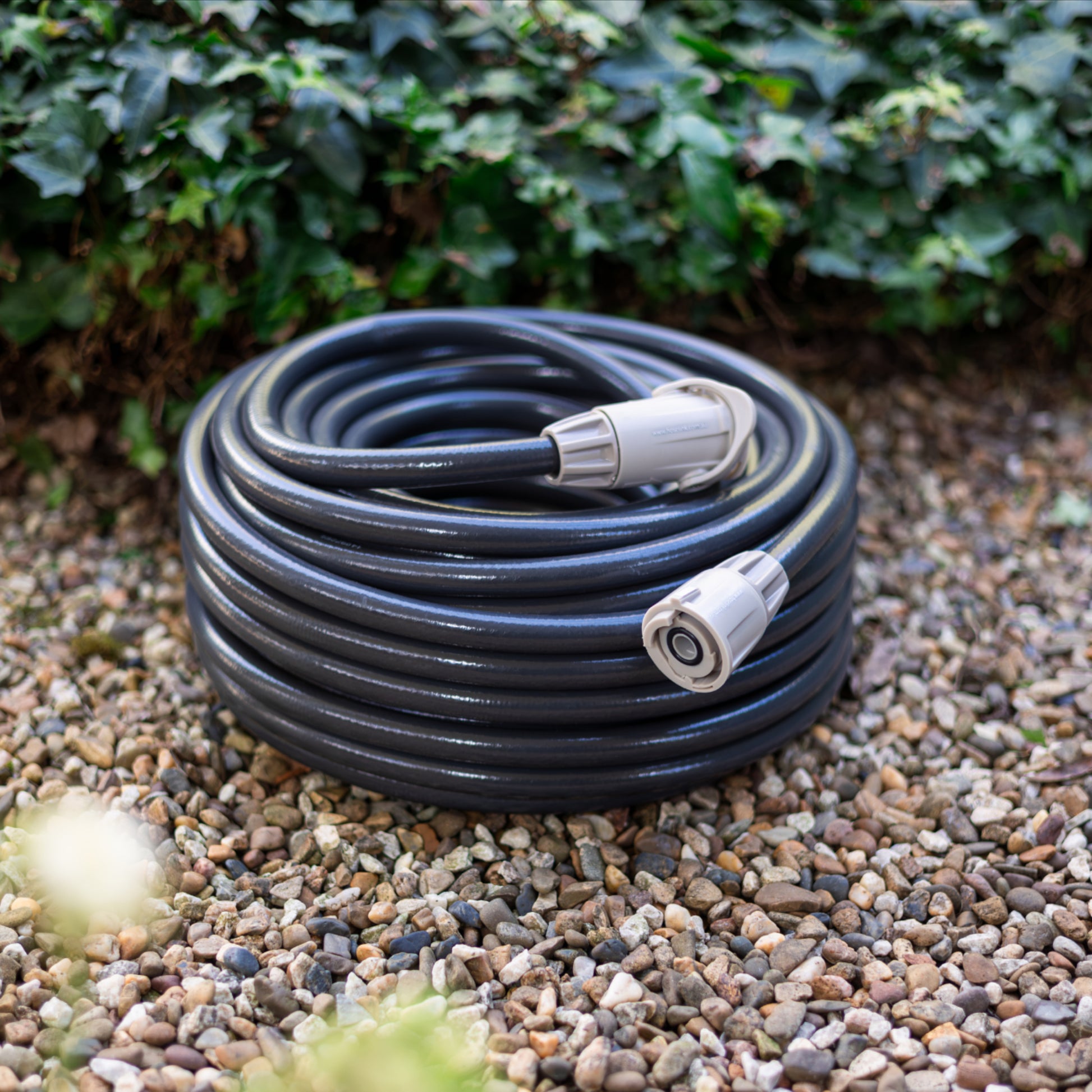 Coiled garden hose on pebbles with green foliage in the background