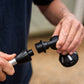 Close-up of a person's hands unscrewing a black plastic garden hose nozzle attachment from a hose, with a blurred outdoor background.