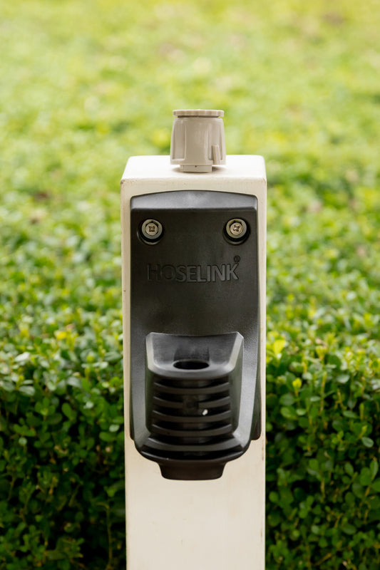 Hose Reel wall bracket mounted to white timber post in garden with Universal Tap Connector on top of post