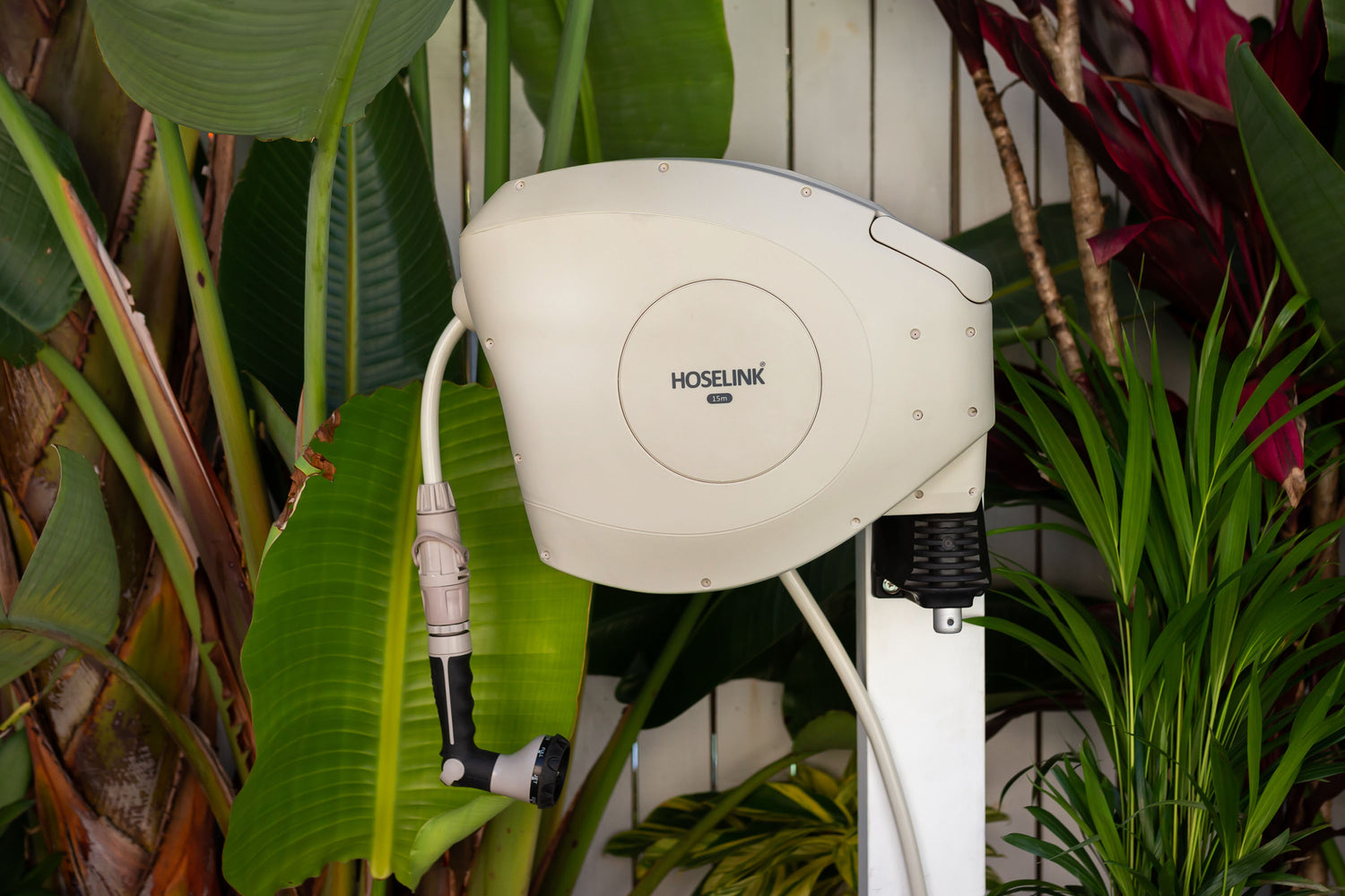 Close-up of Beige Retractable Hose Reel mounted to a white timber post in a tropical garden