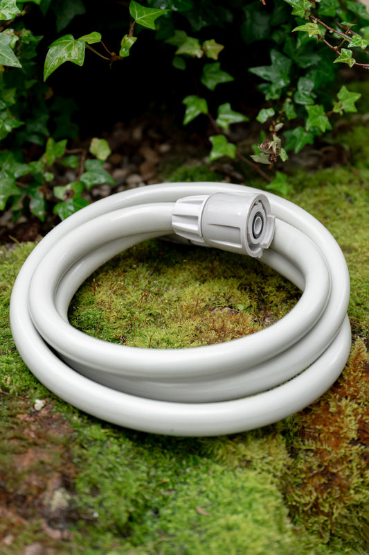 Beige leader hose coiled up neatly sitting on a mossy garden wall