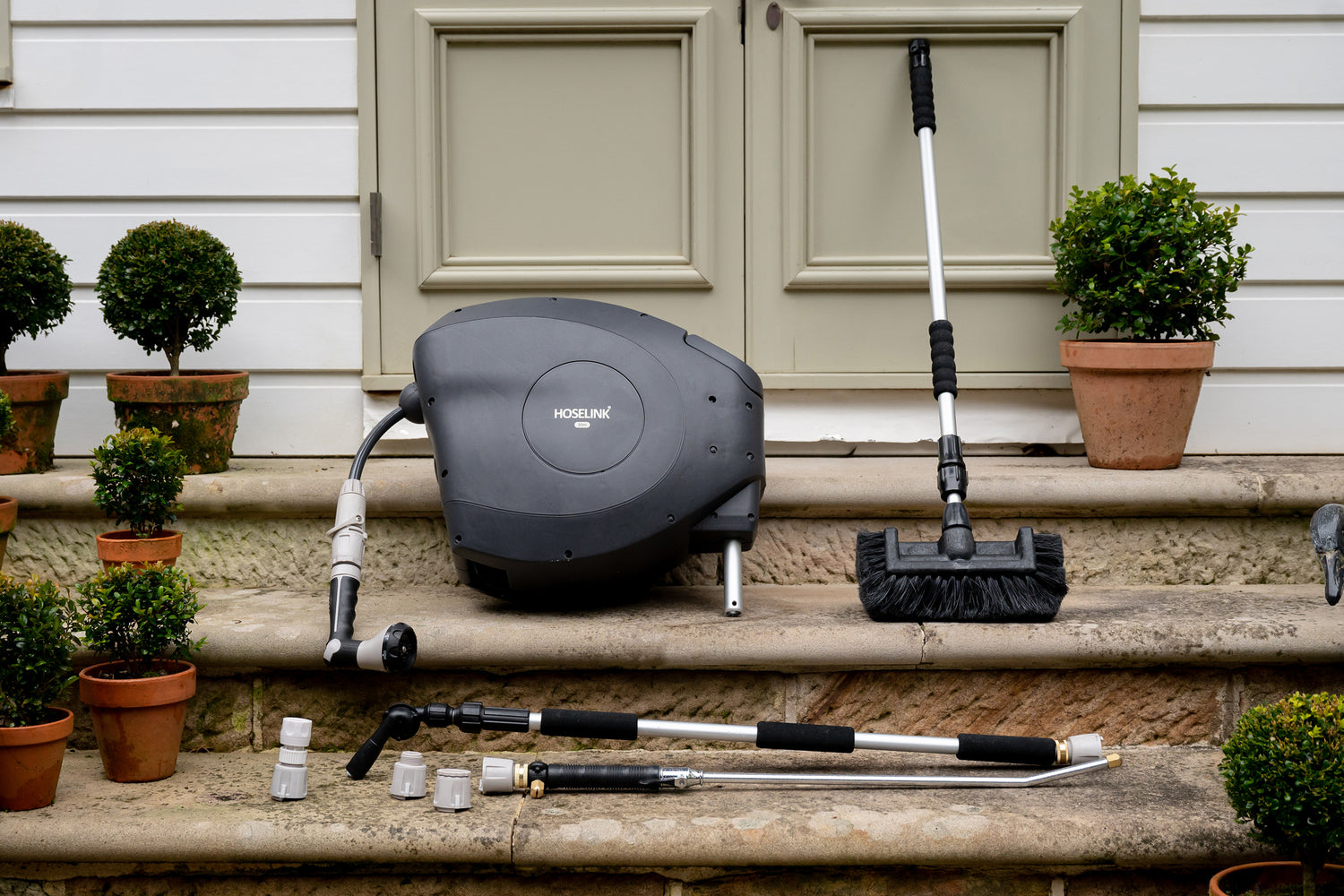 Charcoal Hose Reel sitting on stone steps outside house surrounded by cleaning brush, connectors, the pivot gutter cleaner and super jet washer 