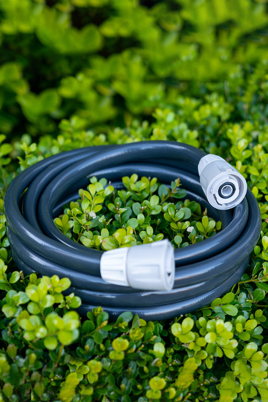 Charcoal leader hose neatly coiled up sitting on top of a green hedge