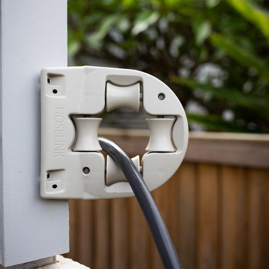 Charcoal-coloured hose fed through a beige hose guide mounted to the corner of a house