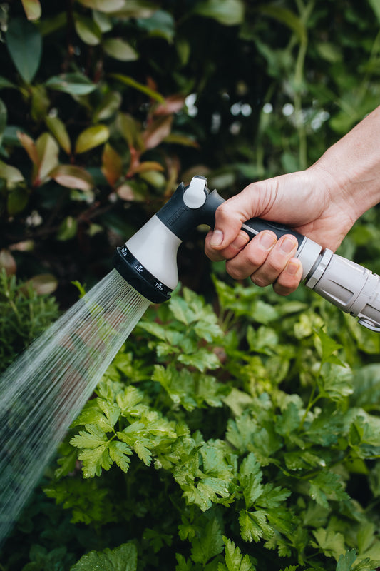Close-up of Comfort 8-Pattern Flow Control sprayer being used to water herbs in a garden with the shower spray setting