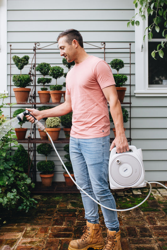 Man Watering Plants With Compact Portable Hose Reel In A Patio