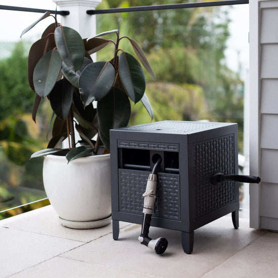 charcoal metal hose reel box on balcony with pot plant next to it