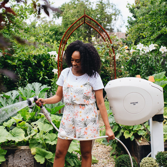 Female in summery outfit watering vegetable garden with Hoselink's Beige Retractable Hose Reel