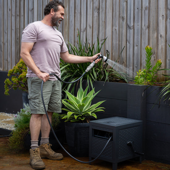 man using charcoal metal hose reel box to water planter boxes in garden