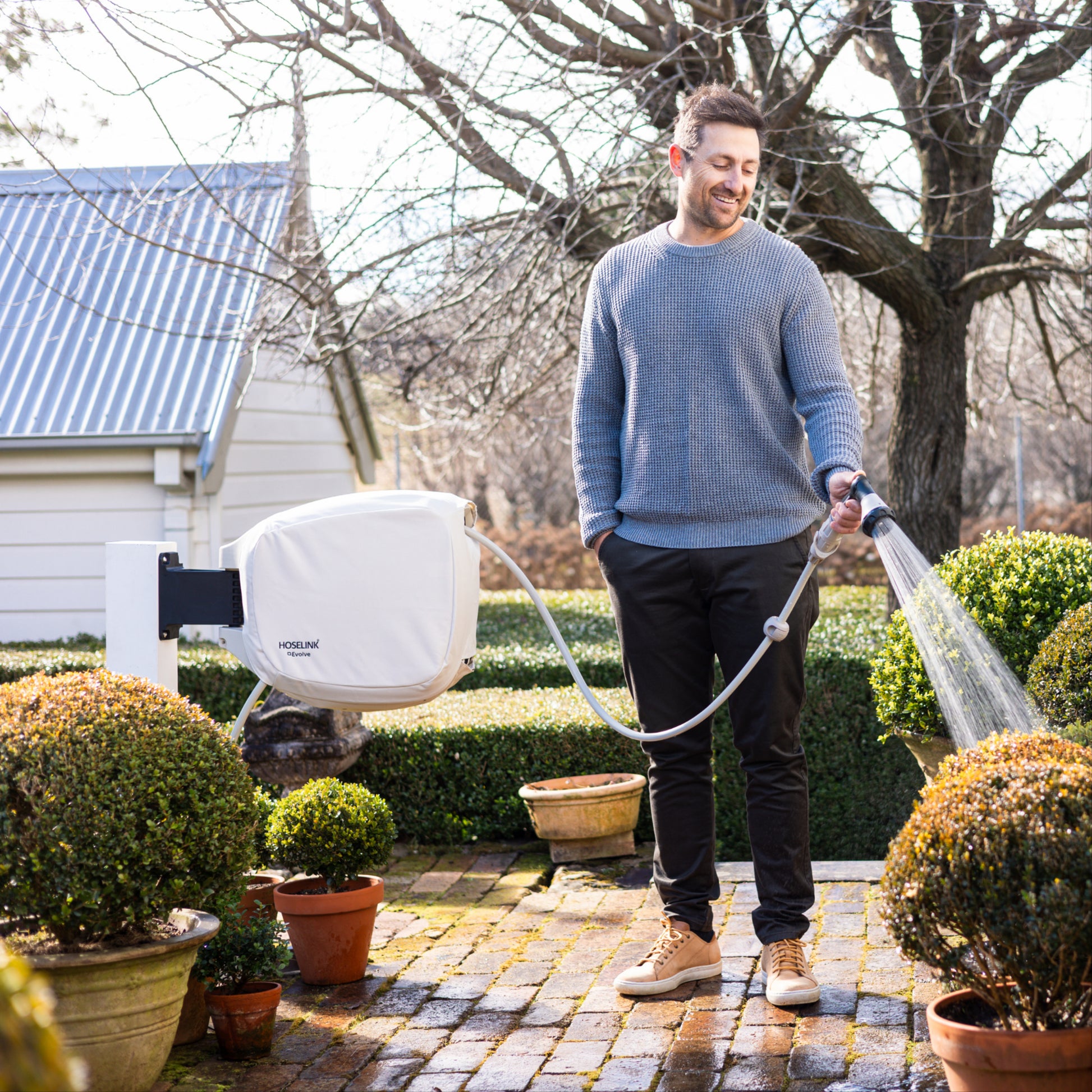 Man using Evolve hose reel with beige cover to water plants in a garden setting