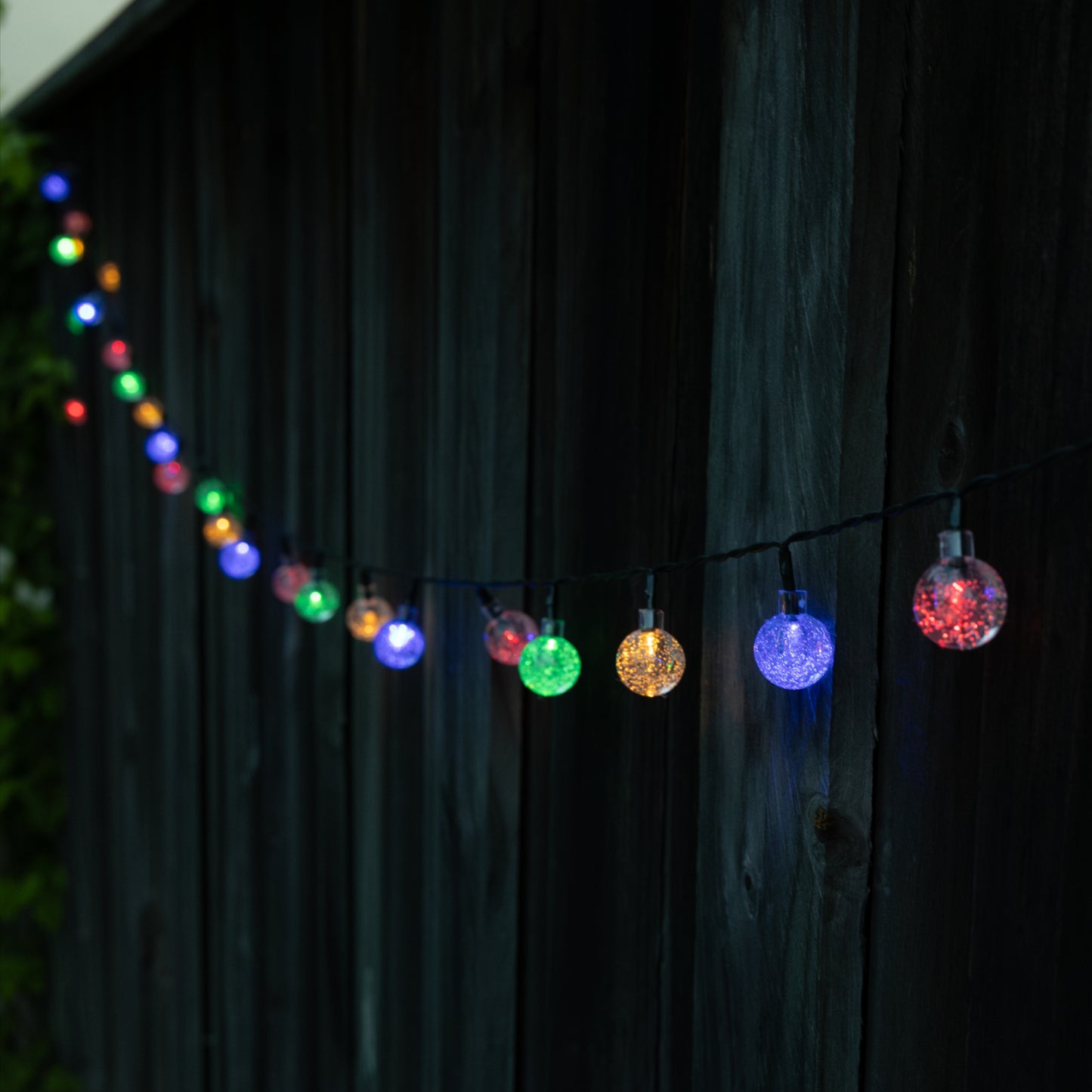 String of colorful outdoor lights against a dark wooden fence