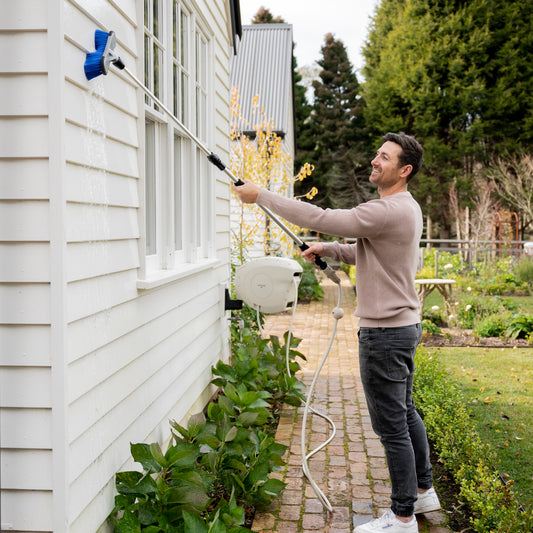 Ben Hayman using extendable cleaning brush to clean white weatherboard house
