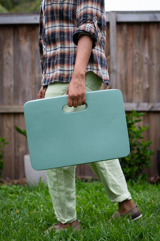 Woman walking across lawn holding Hoselink green soft knee mat