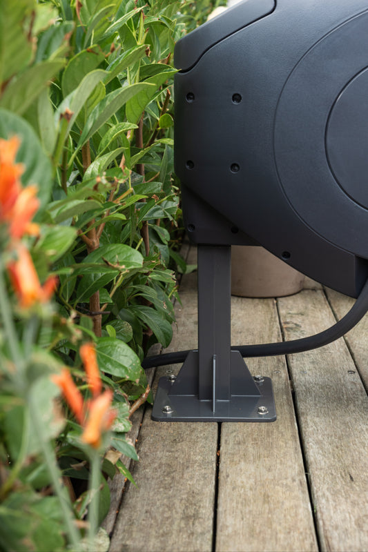 Charcoal classic hoe reel ground mount and reel on a wooden deck with greenery and flowers in the background