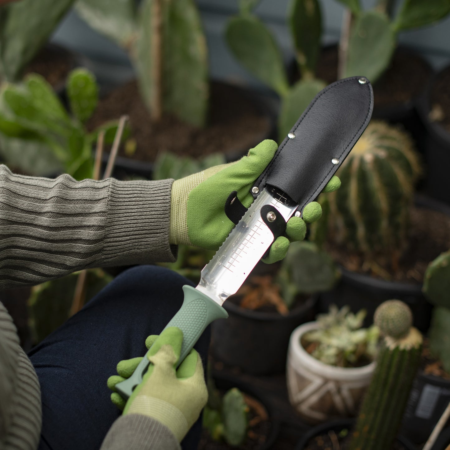 Person holding a stainless steel garden knife with potted plants in the background