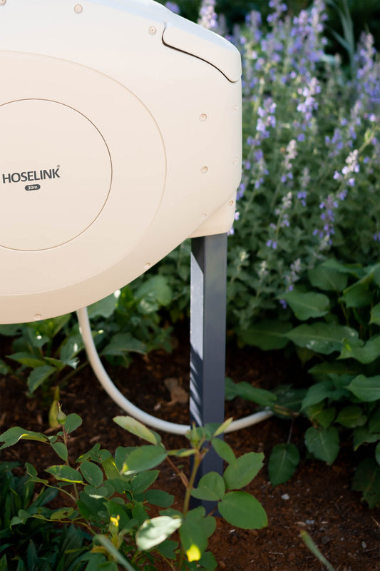 Beige Hose Reel on charcoal metal mounting post in garden setting