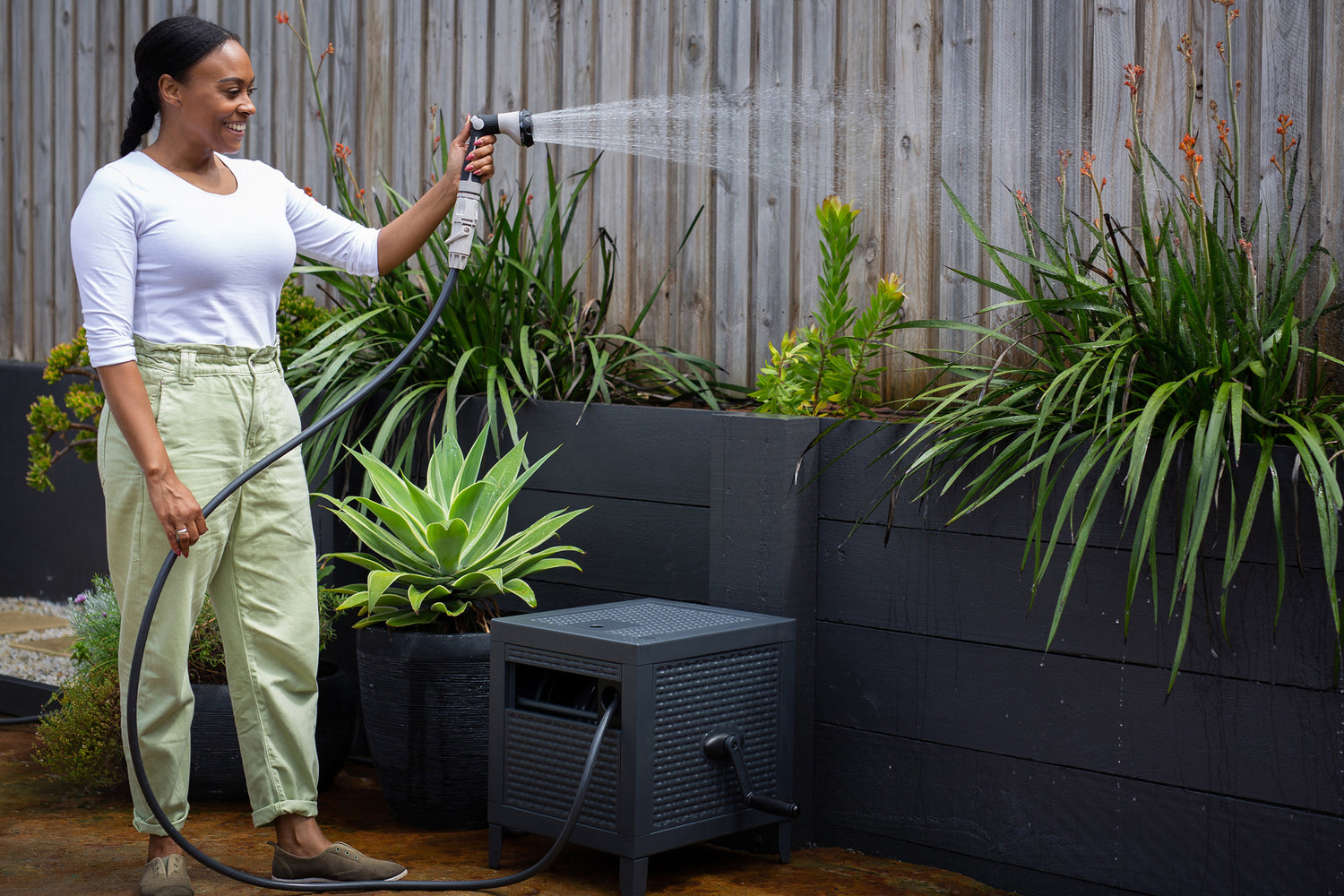 Woman Watering Her Plants With a Charcoal Metal Hose Reel Box