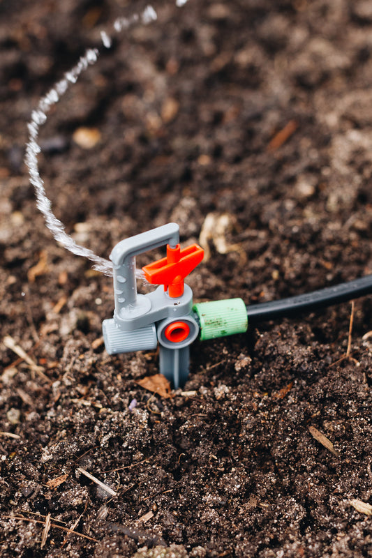 A close up image of a rotor sprinkler head connected on one side to black polypipe, with water streaming from the sprinkler.