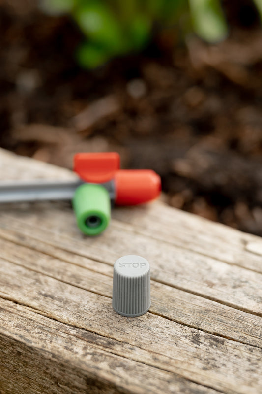 Mini Sprinkler End Cap next to spray nozzle on edge of garden bed