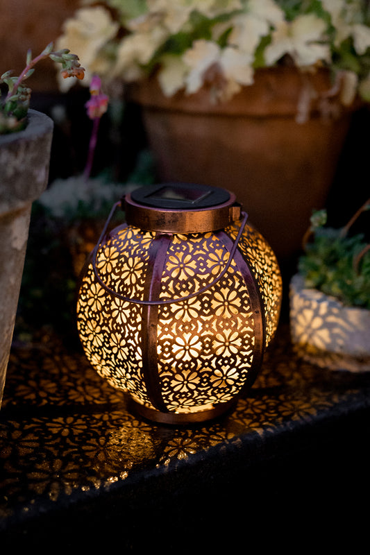 Metal brass-colour Moroccan-style decorative solar light sitting on garden step surrounded by pot plants